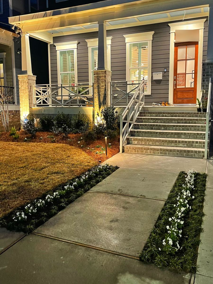 A lit front walk with new beds of white flowers and brick steps at night