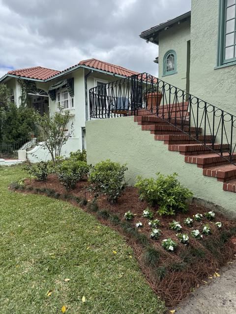 A curved pine-straw bed with shrubs and white impatiens along a stair wall, new sod in front