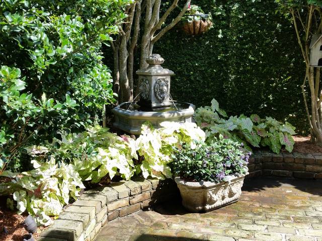 An old-brick courtyard with a tiered fountain, hostas, caladium and a raised brick planter