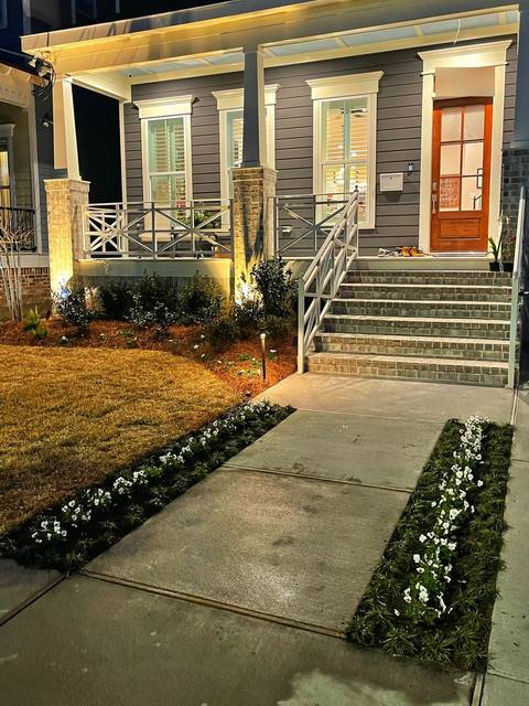 A lit front walk with new beds of white flowers and brick steps at night
