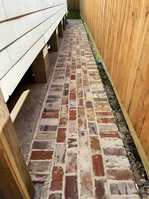 An old-brick walkway between a raised house and a new cedar fence