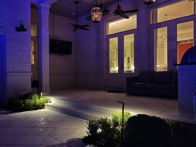 A covered patio at night with gas lanterns and low boxwood with path lights