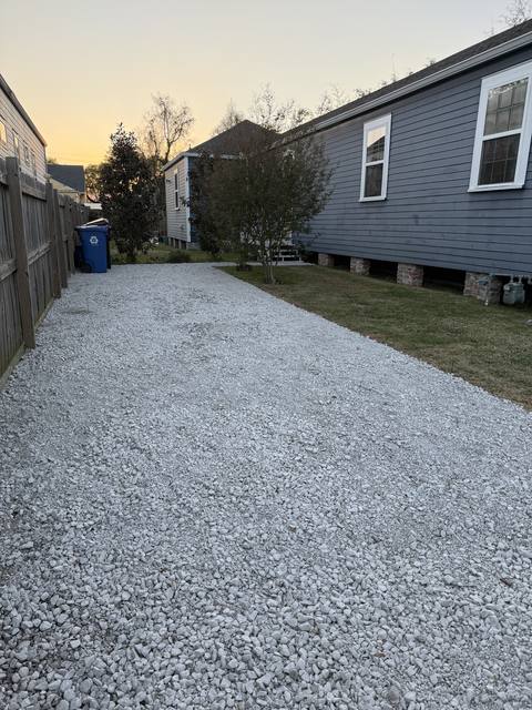 A fresh gravel driveway and a cut lawn beside a raised house at dusk